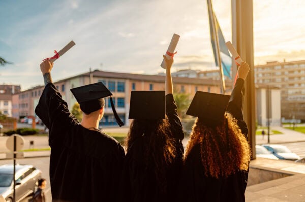 Multiracial graduates raising diplomas, celebrating their academic achievement on graduation day